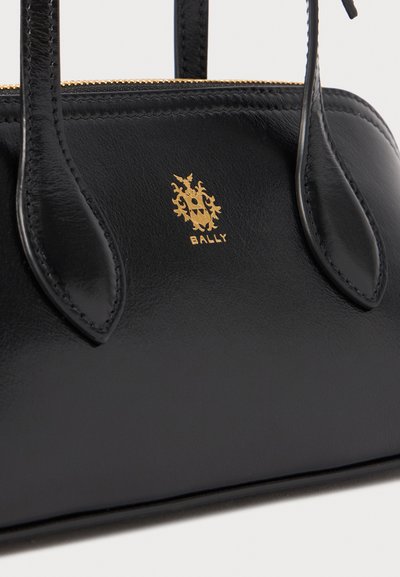 Bolsa de couro preta com um design estruturado, apresentando um logótipo dourado e detalhes em costura, alças duplas e fecho em zíper.