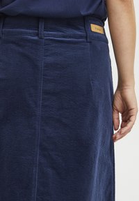 Gonna in corduroy blu navy con texture a righe verticali, spacchi laterali e etichetta beige con il nome del marchio sulla vita.