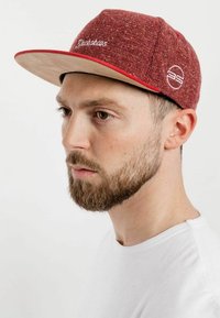 Red and beige cap with a textured fabric, a flat brim, and embroidered logo detail on the front and side.