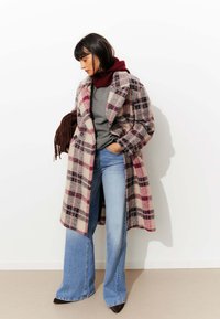 Manteau en laine à carreaux rose, blanc et noir, avec une silhouette longue et décontractée. Assorti avec un pull gris, un jean bleu clair évasé et des chaussures marron.