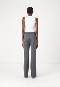 Šedé kalhoty na míru s širokým střihem, svěží bílý top bez rukávů, z pohledu zezadu. Minimalistický styl a hladká textura.