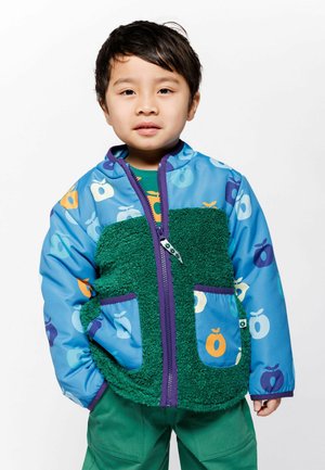 Multifarbige Jacke mit blauer Außenhülle, grünem, flauschigem Vorderteil, Apfelmustern und lila Akzenten. Verfügt über einen Reißverschluss und zwei Vorderfächer.