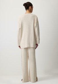 Pulover tricotat bej cu nervuri și pantaloni largi, cu un croi lejer, mâneci lungi și slituri laterale pentru un aspect texturat.