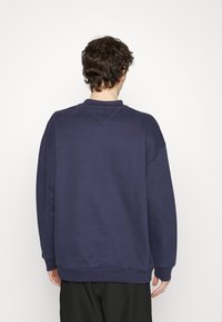 Felpa blu navy con collo a giro, spalle scese e polsini a coste. Presenta una texture morbida e un design semplice e minimalista.