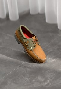Braunes und grünes Lederschuh mit Schnürung, Gummisohle, kontrastierenden Nähten und rotem Innenfutter. Logo an der Seite.