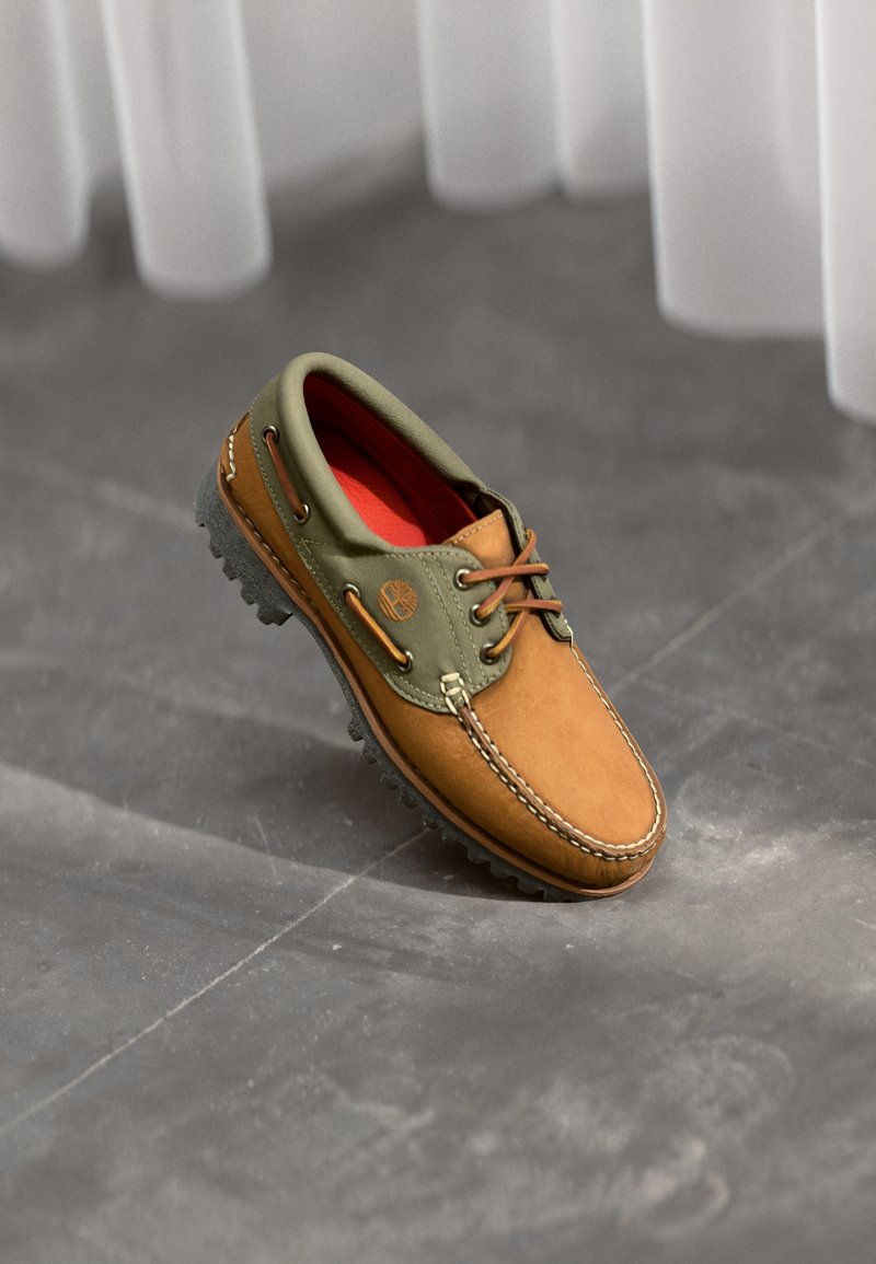 Braunes und grünes Lederschuh mit Schnürung, Gummisohle, kontrastierenden Nähten und rotem Innenfutter. Logo an der Seite.