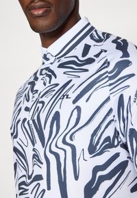 Polo de manga curta com base branca e padrões abstratos em azul marinho, com pala de três botões e detalhes de gola listrada.