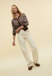Pruhovaný cardigan v hnědé a krémové barvě, bílé džíny s vysokým pasem, hnědé tenisky, minimalistický design, hladká textura, neutrální pozadí.