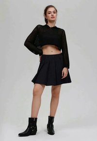 Svart kort topp i mesh med långa ärmar, kombinerad med en utsvängd svart kjol med kritstrecksrand och svarta ankelstövlar med dekorativa detaljer.