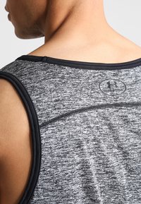 Hombre vistiendo una camiseta deportiva sin mangas de Under Armour en gris y negro, mostrando la parte superior de la espalda y el área del cuello.
