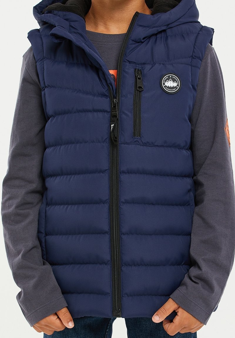 Veste sans manches matelassée bleu marine avec fermeture éclair à l'avant, capuche et logo patch. Présente un design matelassé horizontal et deux poches zippées.