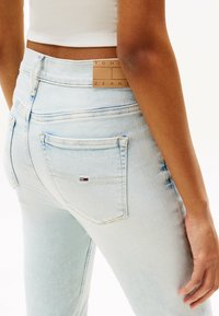 Jeans de tiro alto en azul claro con una textura suave. Incluyen un parche de marca de cuero y un pequeño logo en el bolsillo trasero.