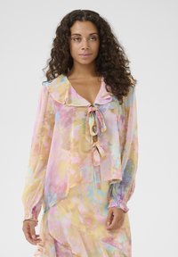 Blusa trasparente e multicolore con morbide tonalità pastello, colletto arricciato, chiusura con fiocco sul davanti e polsini elasticizzati. Leggera con un design fluido.