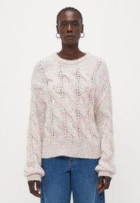 Pulover din tricot în roz deschis, cu un model cu cabluri, manșete răsucite și guler rotund, asortat cu blugi albaștri. Fir texturat cu un aspect delicat.