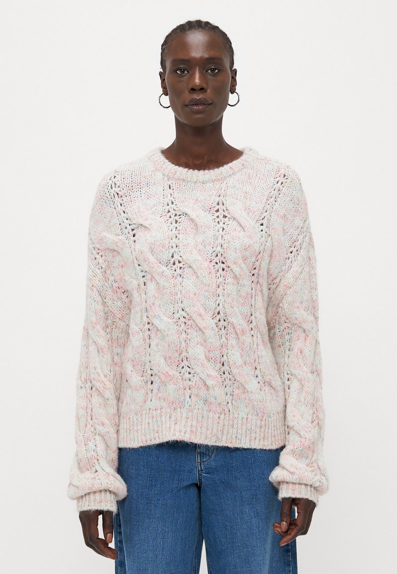 Pulover din tricot în roz deschis, cu un model cu cabluri, manșete răsucite și guler rotund, asortat cu blugi albaștri. Fir texturat cu un aspect delicat.