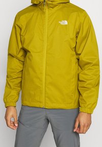 Chaqueta impermeable amarilla con capucha, con puños elásticos y cremallera frontal. Logotipo en el lado izquierdo del pecho, textura suave y corte regular.