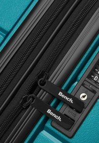 Valigia teal con cerniere nere e doppie cerniere con il marchio "Bench". Include una serratura a combinazione numerica e una superficie testurizzata.