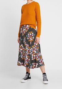 Orange texturerad tröja i kombination med en svart blommig kjol med färgglada mönster. Sammanfattat med svarta högskor.