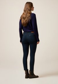 Suéter navy y jeans skinny de color azul oscuro, con una cinturilla que presenta un parche de cuero, combinados con botines negros.