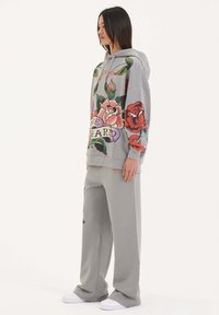 Grå hoodie med färgglada blommönster och text, i kombination med matchande grå vida byxor och vita sneakers. Slät, mjuk textur.