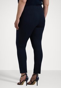 Mörkblå passande byxor med ett mjukt, stretchigt material och en elegant design. Har en bakseam och är kombinerad med trendiga högklackade sandaler.