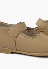 Tan leren schoenen met een ronde neus, gegolfde randdetails en een klittenbandsluiting. Platte zolen met subtiele stikselaccenten.