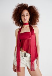 Červený saténový halter top s vrstveným dizajnom a strapcovým detailom, spárovaný s svetlosfarbenou mini sukňou so bočným zipsom a opaskom.