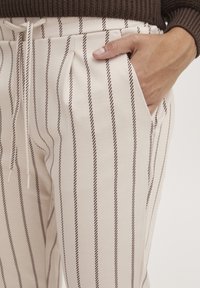 Krämfärgade byxor med bruna vertikala ränder, med elastisk midja, dragsko och sidofickor. Mjuk bomullstyg med avslappnad passform.