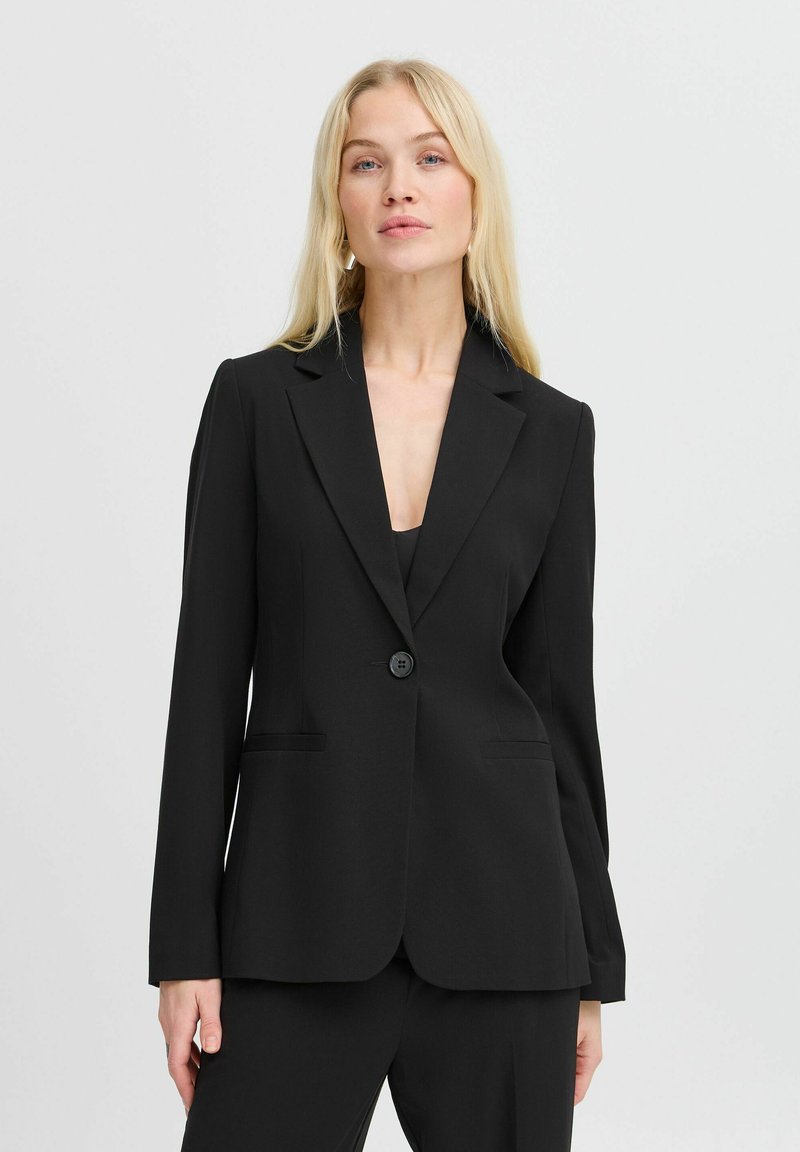Blazer noir avec une coupe ajustée, revers en pointe, fermeture à un bouton et poches latérales. Texture lisse et design épuré.