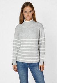 Grauer gestreifter Pullover mit hohem Kragen, versehen mit weißen horizontalen Streifen, gerippten Bündchen und seitlichen Schlitzen, kombiniert mit blauen Jeans.