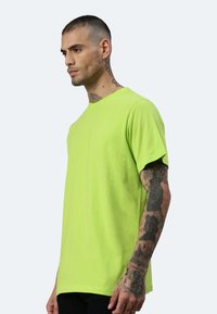 T-shirt in cotone verde brillante con collo a giro e maniche corte. Presenta una vestibilità ampia e una texture morbida, mostrato su un modello di profilo.