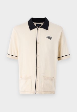 Krótki kardigan z krótkim rękawem w jasnym beżu z czarnym kołnierzykiem, haftowanym logo i dwoma przednimi kieszeniami. Wykonany z miękkiego materiału dzianinowego.
