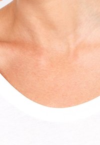 Gros plan sur un t-shirt blanc à col rond, révélant une texture de peau lisse au niveau du cou et de la clavicule, avec un ton de peau naturel et subtil.
