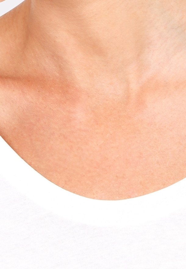 Gros plan sur un t-shirt blanc à col rond, révélant une texture de peau lisse au niveau du cou et de la clavicule, avec un ton de peau naturel et subtil.