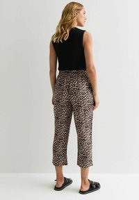 Zwarte mouwloze top gecombineerd met beige pantacourts met luipaardprint. Broek heeft een elastische tailleband en zijzakken. Zwarte instapsandalen.