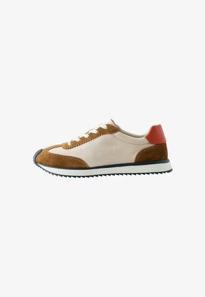 Niskoprofilowy sneaker z beżowej skóry i brązowymi panelami z zamszu, białymi sznurowadłami, czerwonym akcentem na pięcie oraz żłobioną czarno-białą podeszwą.