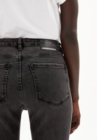 Jeans de mezclilla negra con un corte de cintura alta, bolsillos traseros y una etiqueta de marca en la cintura. Textura suave con un ligero desvanecimiento.