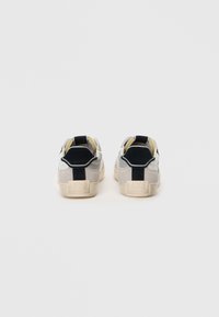 Sneakers grigi e neri con una finitura in suede texture, caratterizzati da un design low-top, dettagli gialli e un'etichetta posteriore con la scritta "1973."