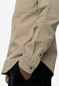 Beige Hemd mit Knöpfen, aus Baumwollmischung, mit einer Brusttasche und geknöpften Manschetten, kombiniert mit strukturierten, dunkelblauen Cordhosen.