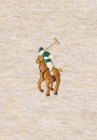 Broderad polo-spelare på häst i brunt, grönt och blått på en beige texturerad tygbakgrund. Detaljerad sömnad framhäver designen.