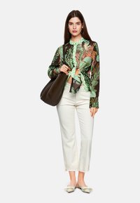 Long-sleeve, button-up shirt with green and brown floral print, tied at the waist, paired with white wide-leg pants and flat beige shoes.