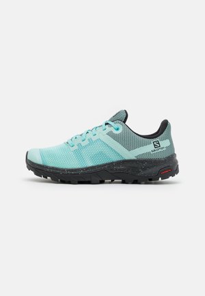 Chaussure de trail running bleu clair et noire avec empeigne en mesh, lacets, et semelle robuste équipée de la technologie Contagrip de Salomon, vue de côté.