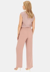 Jasnoróżowa bluzka bez rękawów z teksturowanej tkaniny, połączona z szerokimi różowymi spodniami. Modelka nosi cieliste szpilki. Widok z tyłu.