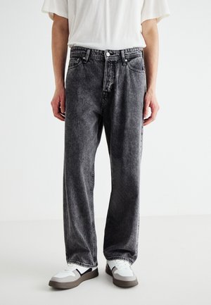 Zwarte spijkerbroek met een losse pasvorm, verweerde afwerking, vijf zakken, knoopsluiting en contrasterende stiksels, gecombineerd met witte sneakers.