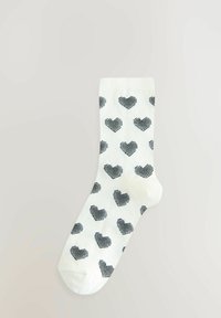 Witte sok met zwarte gestreepte hartpatronen. Heeft een geribde bovenkant en een gladde textuur. Enkel lengte ontwerp geschikt voor casual draag.