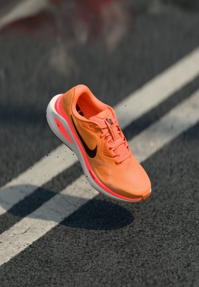 Nike Laufschuh aus leuchtend orangefarbenem Netzmaterial mit einem schwarzen Swoosh, ausgestattet mit einem gepolsterten Kragen und einer weißen Zwischensohle, schwebt über Asphalt.