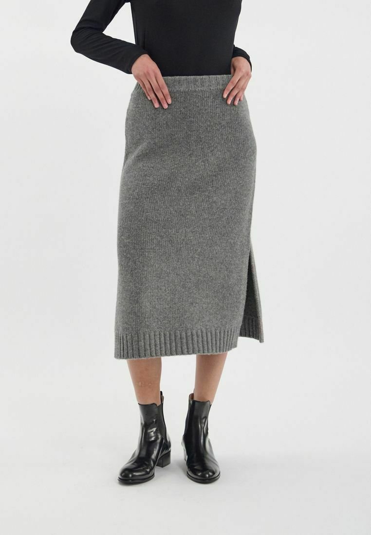 Jupe midi tricotée grise avec fente latérale, dotée d'une taille côtelée. Associée à des bottines noires, sur un fond blanc uni.