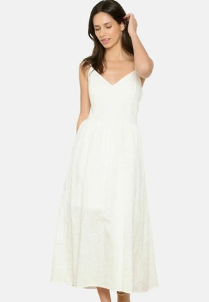 Weißes Midikleid mit V-Ausschnitt, ärmellosem Design und kreisförmigem Cut-out-Muster, das einen taillierten Oberteil und einen fließenden Rock hat.