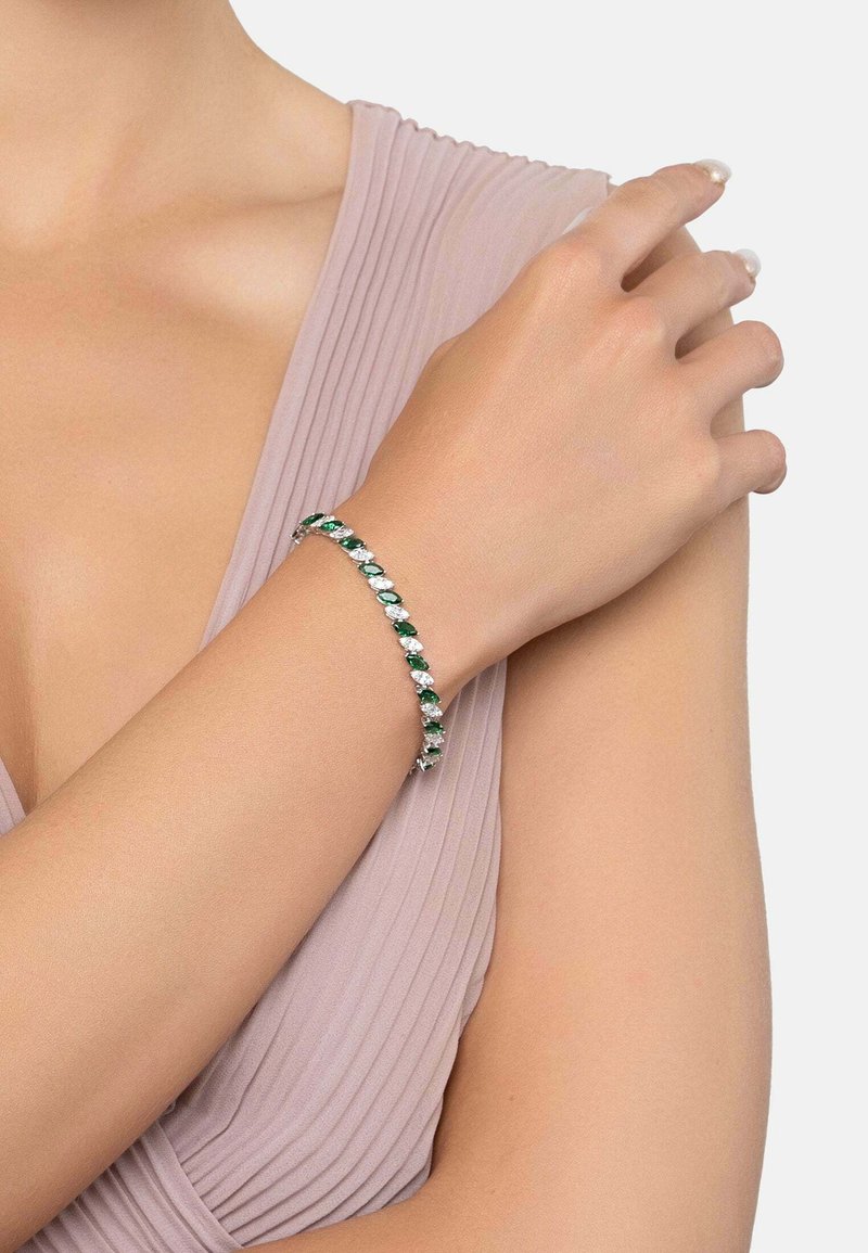 Silver bracelet with alternating green and clear gemstones, featuring a sleek design and smooth texture, worn on a bare arm.