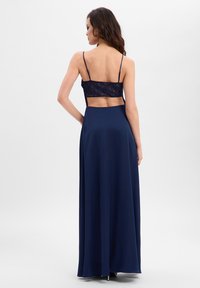Robe de soirée bleu marine avec un corsage en dentelle, un dos nu et une longue jupe fluide. Bretelles spaghetti ajustables et texture lisse.